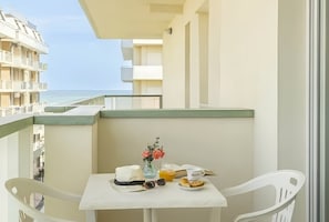 Ein Balkon mit Frühstückstisch, Blumen in einer Vase und Blick auf das Meer.