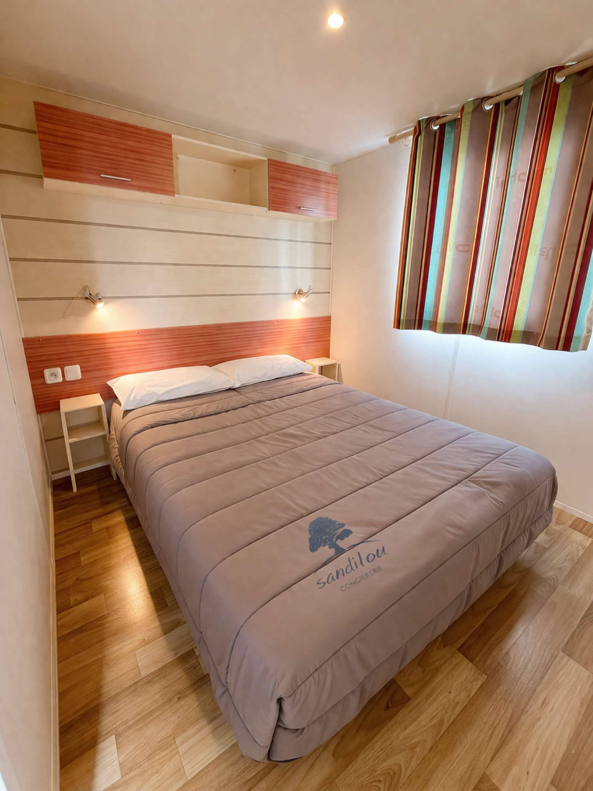 Une chambre à coucher avec un lit, des tables de chevet, une tête de lit, une fenêtre avec des rideaux et un plancher en bois.