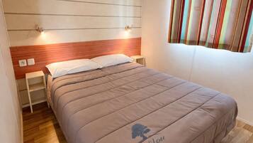 Une chambre à coucher avec un lit, des tables de chevet, une tête de lit, une fenêtre avec des rideaux et un plancher en bois.