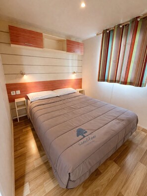 Une chambre à coucher avec un lit, des tables de chevet, une tête de lit, une fenêtre avec des rideaux et un plancher en bois.