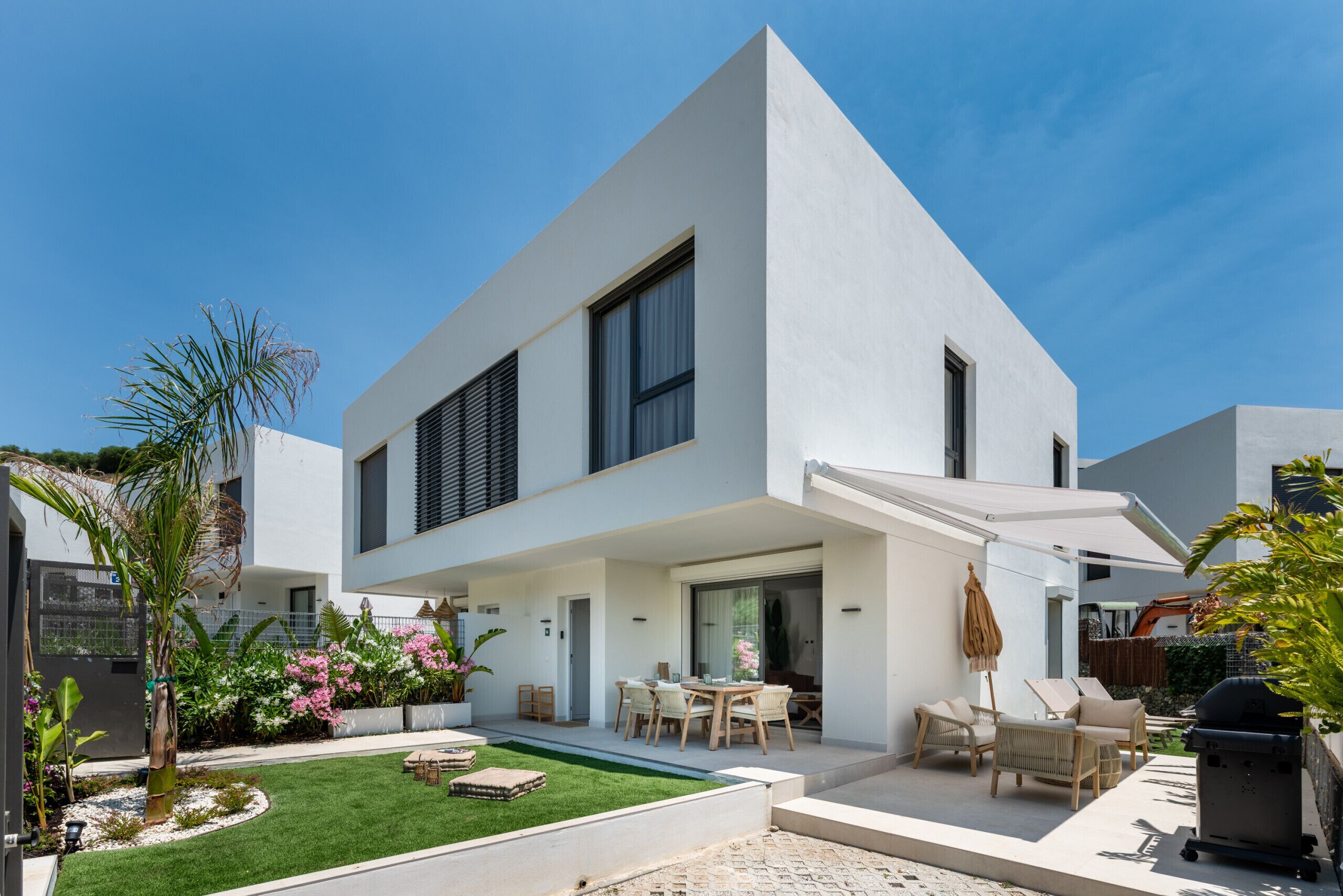 A modern two-story house with a patio, outdoor seating, and a barbecue area.