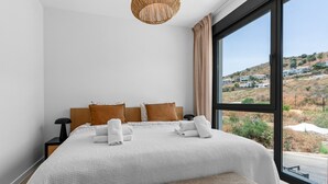 A bedroom with a large bed, a view of a hilly landscape, and a window with curtains. - 7 - Bright house with private plunge pool (Mijas)