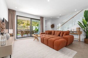 Ein modernes Wohnzimmer mit einer Eckcouch, einem Essbereich mit Tisch und Stühlen sowie einer großen Schiebeglastür, die auf eine Terrasse im Freien führt.