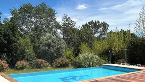 Una piscina con cubierta de madera, rodeada de abundante vegetación y árboles.