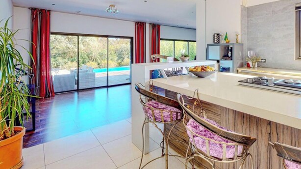 Una cocina moderna con una isla grande, taburetes de bar y vistas a una piscina.