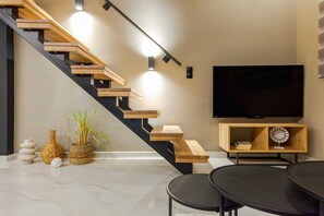A modern living room with a staircase, a flat-screen TV, a round table, and decorative items. - Chrysma Urban Living 1, Apartment (Rhodes)