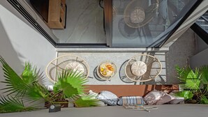 Een balkon met drie rieten stoelen, een tafeltje met eten en verschillende potplanten.