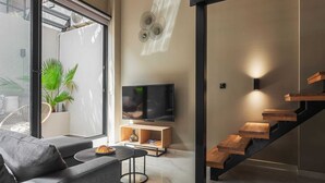 Een moderne woonkamer met een bank, een salontafel, een televisie, een trap en een potplant.