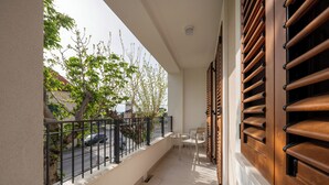 A balcony with a view of a street, a tree, and a building. There are two chairs and a small table.
