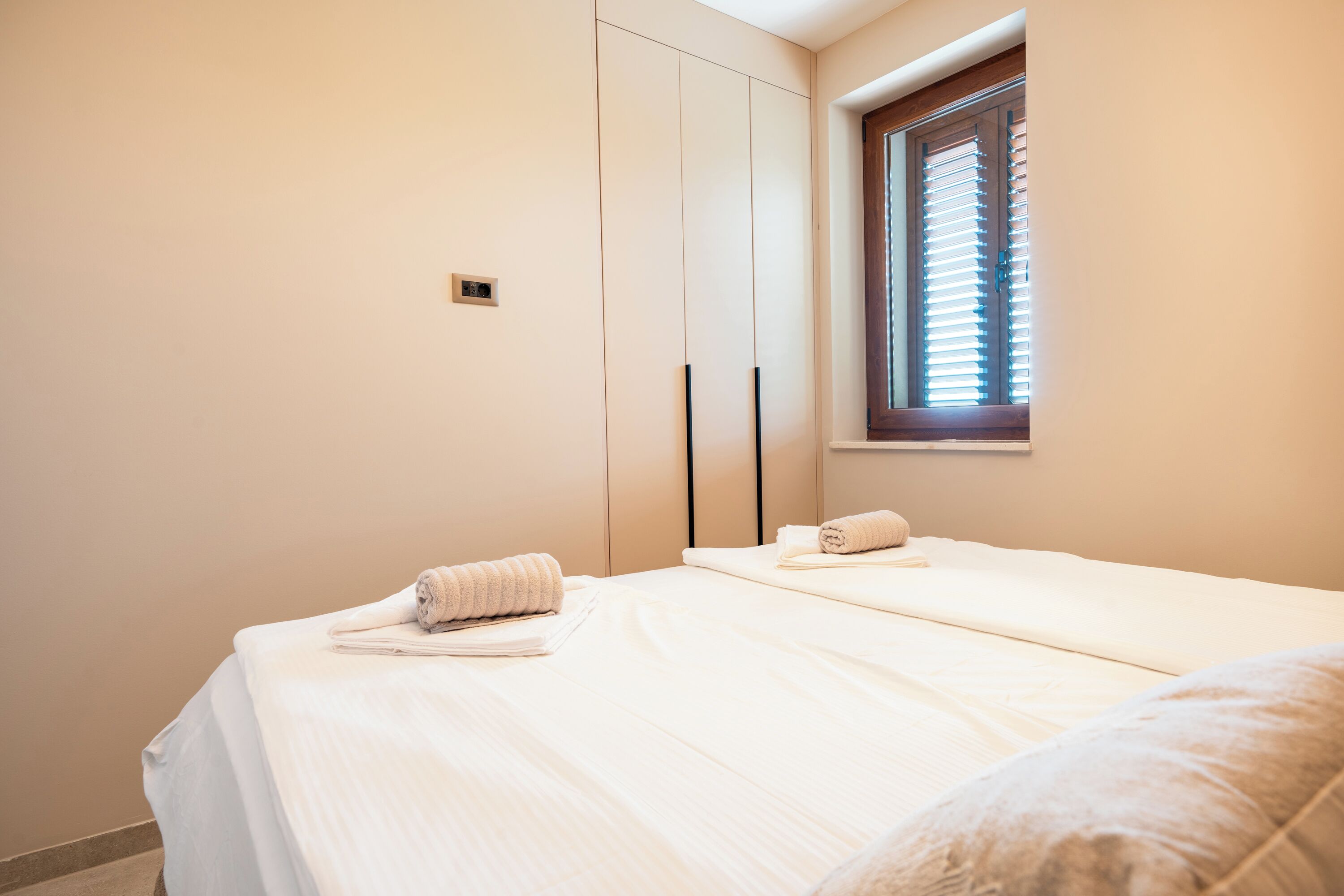 Une chambre avec deux lits, une fenêtre avec des stores et un interrupteur fixé au mur.