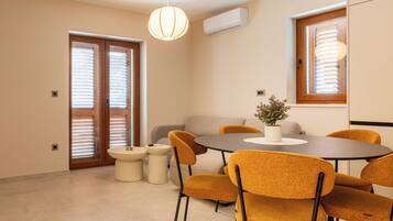 Uma sala de jantar com uma mesa redonda, seis cadeiras, uma mesinha lateral e um vaso com planta.