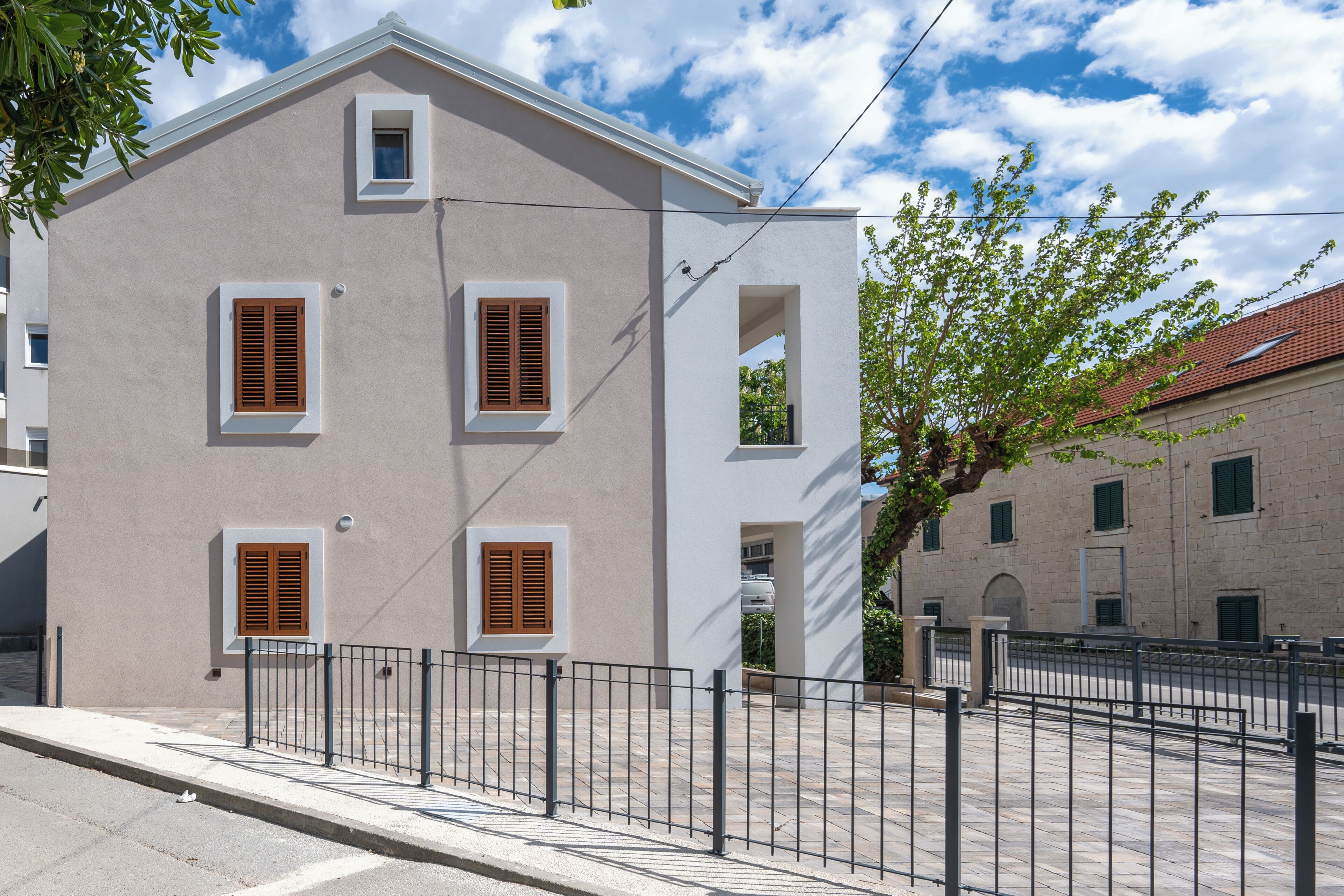 A two-story building with a flat facade, multiple windows with shutters, a metal fence in front, and a clear sky.