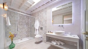 A modern bathroom with a glass shower enclosure, a white toilet, a large sink with a mirror above, and a vase with flowers on the floor. - Amarada Nostalgia City Suite, Αpartment (Rhodes)