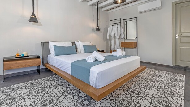A modern hotel room with a large bed, bedside tables, a wardrobe, and a ceiling with exposed beams. - Amarada Nostalgia City Suite, Αpartment (Rhodes)