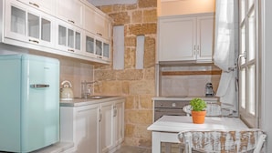 A compact kitchen with white cabinets, a blue refrigerator, a stove, and a small table with a potted plant. - Amarada Nostalgia City Suite, Αpartment (Rhodes)