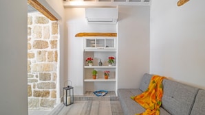 A cozy living area with a stone wall, a white built-in shelf with red flowers, a grey sofa with a colorful throw, and a black lantern. - Amarada Nostalgia City Suite, Αpartment (Rhodes)