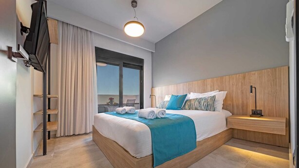 Ein modernes Hotelzimmer mit einem großen Bett, einem Nachttisch, einem Fernseher und einem Fenster mit Vorhängen.