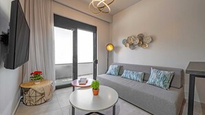 Ein modernes Wohnzimmer mit einem grauen Sofa, einem runden Couchtisch, einer Stehlampe und einem an der Wand befestigten Fernseher.