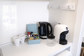 Eine Küchenzeile mit Kaffeemaschine, Wasserkocher, Tasse und einer kleinen Auswahl an Snacks.