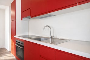 Eine moderne Küche mit roten Schränken, einer Edelstahl-Spüle und einem eingebauten Ofen.