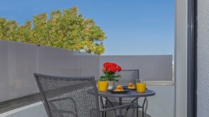 Een balkon met een tafel, stoelen, een plant in pot en een glas sinaasappelsap.