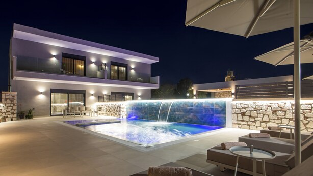 Un bâtiment moderne à deux étages doté d’une piscine, d’un espace extérieur aménagé et d’une cascade.