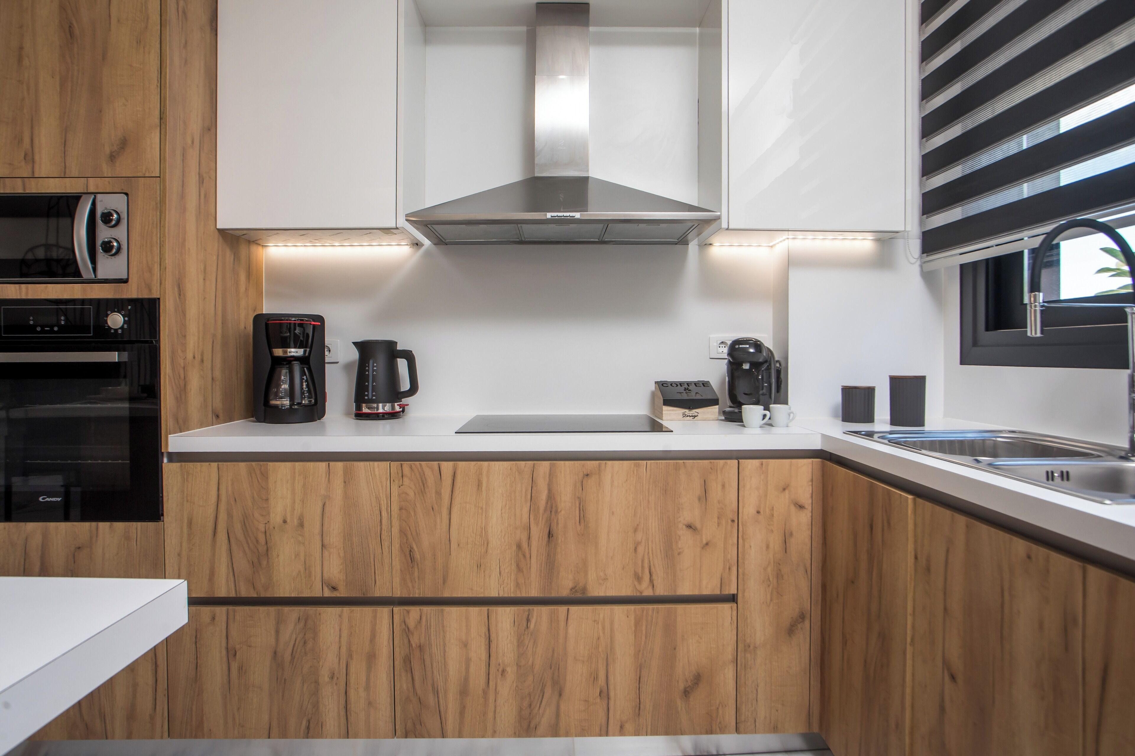 A modern kitchen with wooden cabinets, a stainless steel range hood, a coffee maker, and a built-in oven.