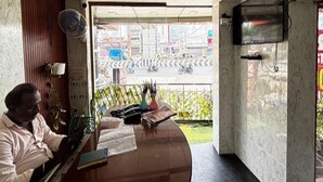 A reception desk with a man seated, a television mounted on the wall, and a view of the street outside.
