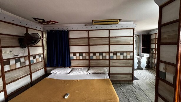 A room with a bed, a fan, a curtain, and a small table.