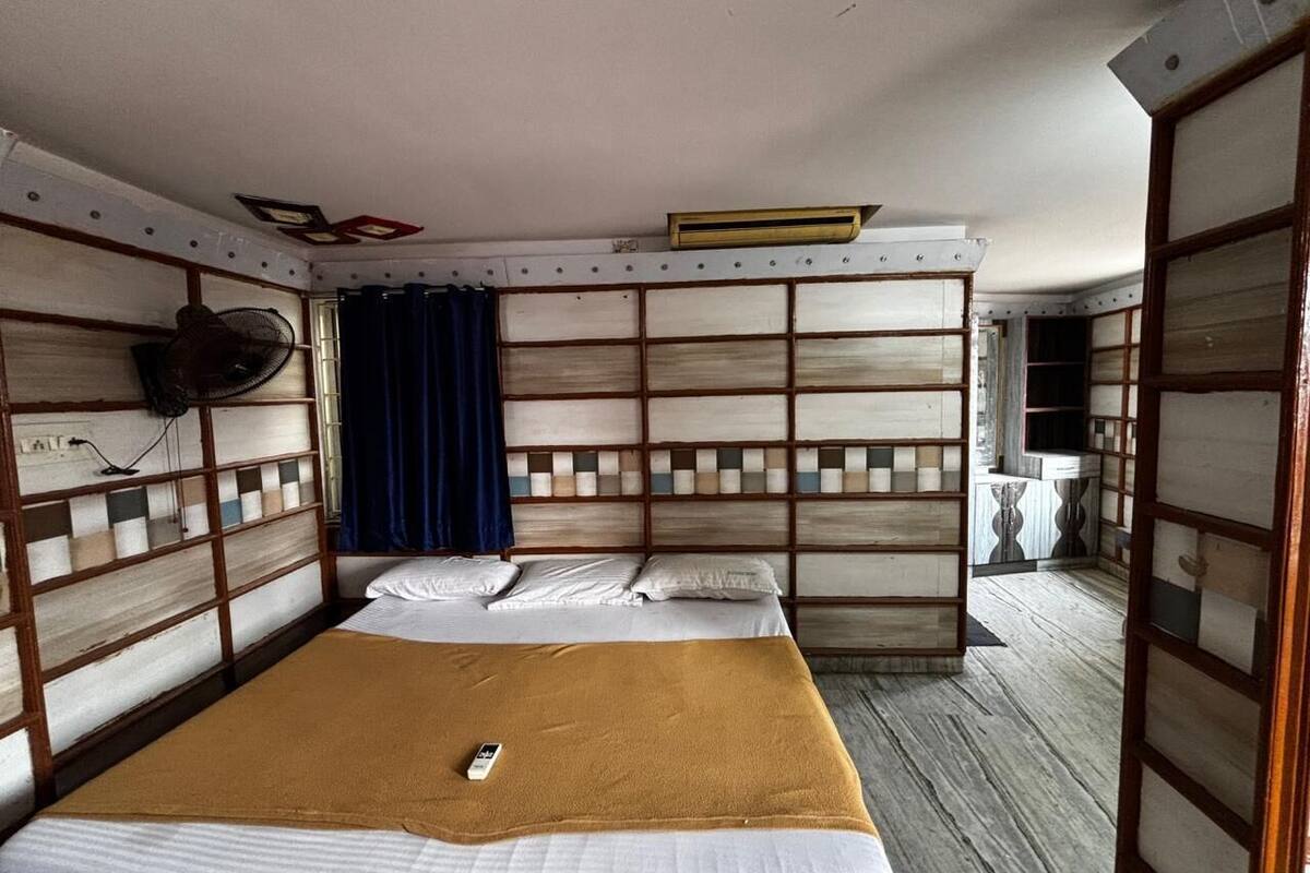 A room with a bed, a fan, a curtain, and a small table.