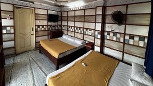 A room with two beds, a door, a ceiling fan, and a wall-mounted TV.