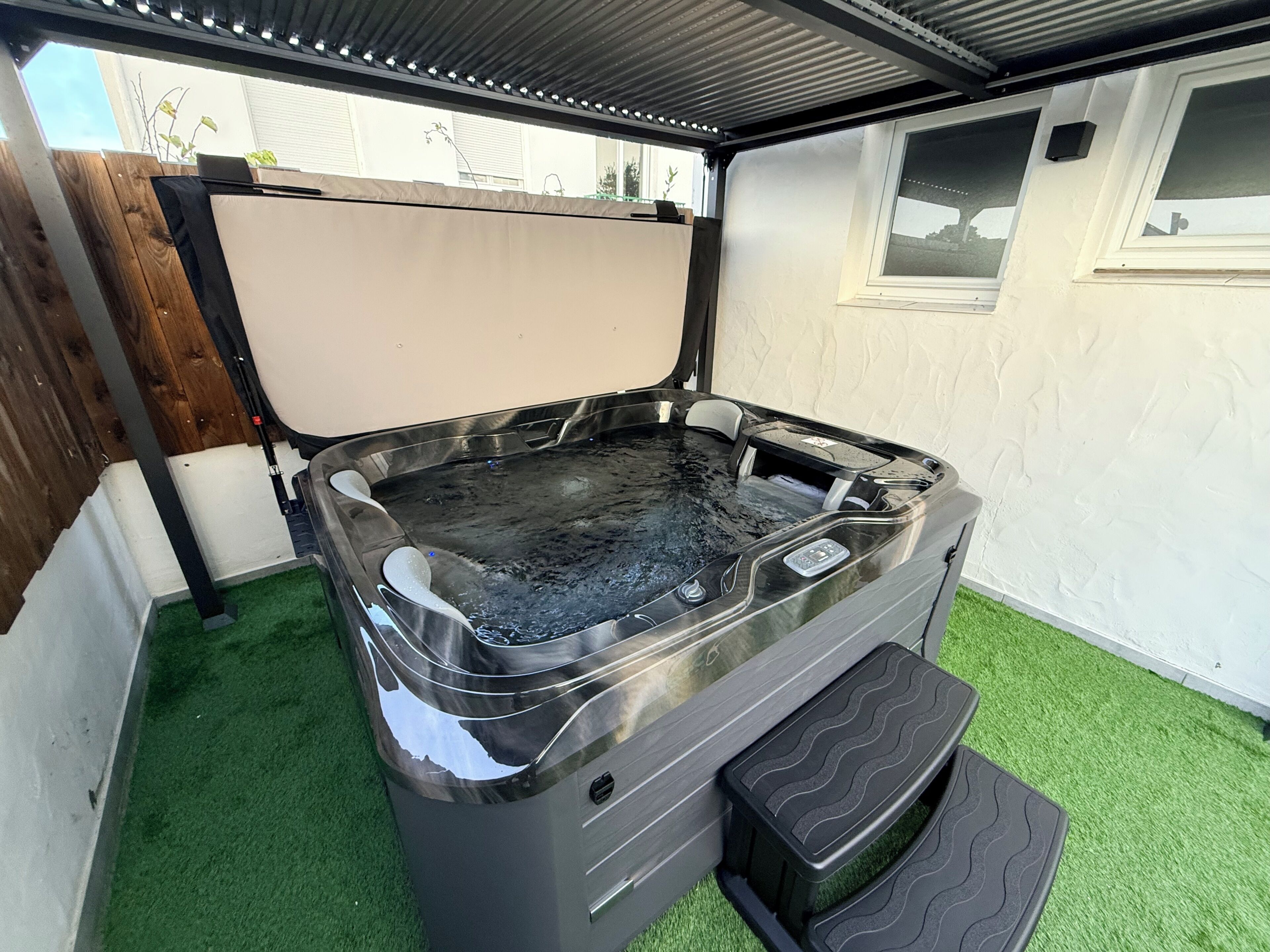Un bain à remous doté d’un panneau de commande, d’un petit marchepied et d’un écran blanc.