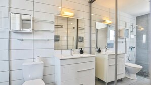 Un bagno moderno con il water, due lavabi, uno specchio e una doccia.