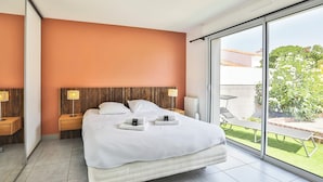 Una moderna camera d'albergo con un letto grande, due comodini con lampade, una porta scorrevole in vetro verso un balcone e vista sull'esterno.