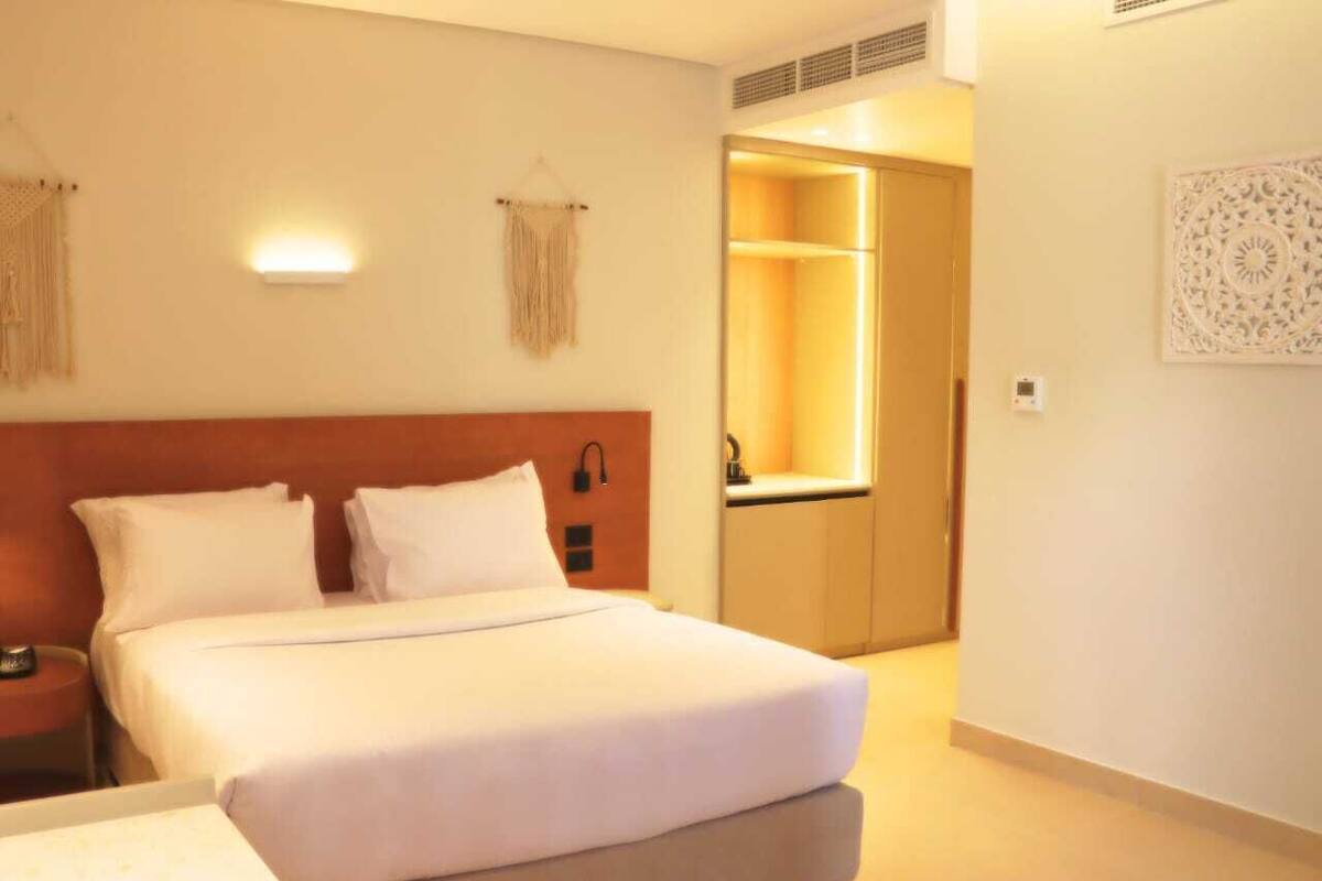 A hotel room with a bed, bedside tables, a wardrobe, and a wall-mounted light fixture.