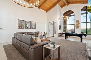 Ein geräumiges Wohnzimmer mit einer Ledersofa, einem Billardtisch und großen Fenstern mit Blick ins Freie.