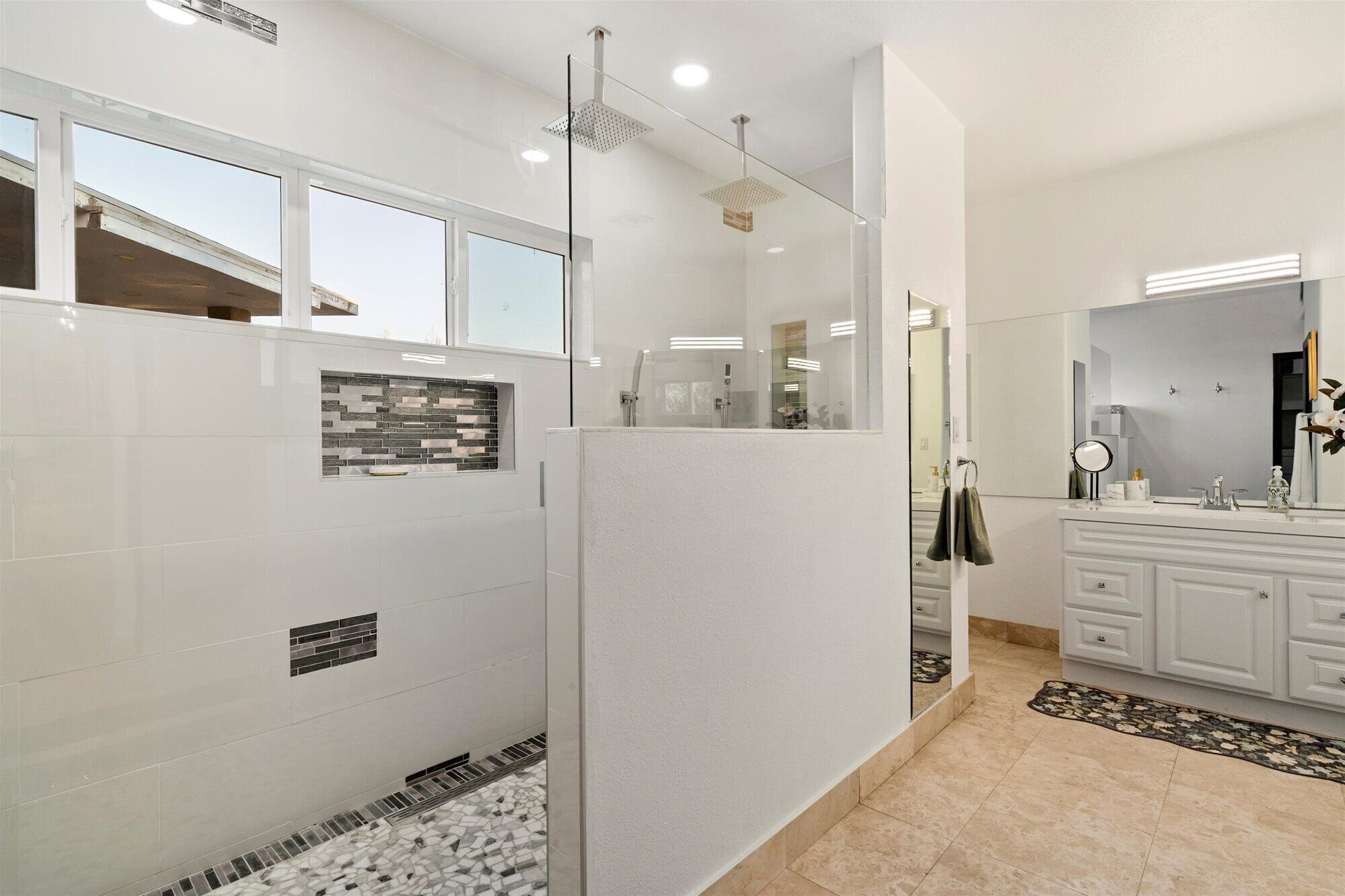 A modern bathroom with a glass shower enclosure, a white vanity with a mirror, and a tiled floor.