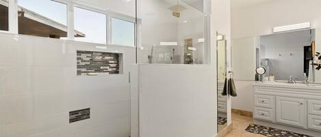 A modern bathroom with a glass shower enclosure, a white vanity with a mirror, and a tiled floor.