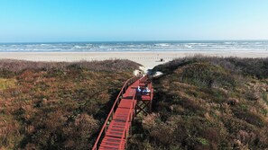 Ein hölzerner Steg führt zu einem Strand mit freiem Blick auf das Meer.