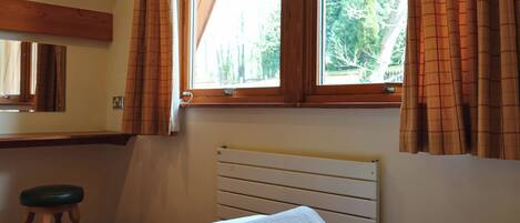 A bedroom with a bed, a window with curtains, a radiator, and a wooden stool.