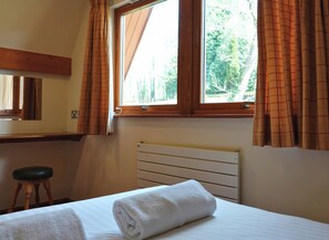 A bedroom with a bed, a window with curtains, a radiator, and a wooden stool. - Bracken Lodge (Newton Abbot)