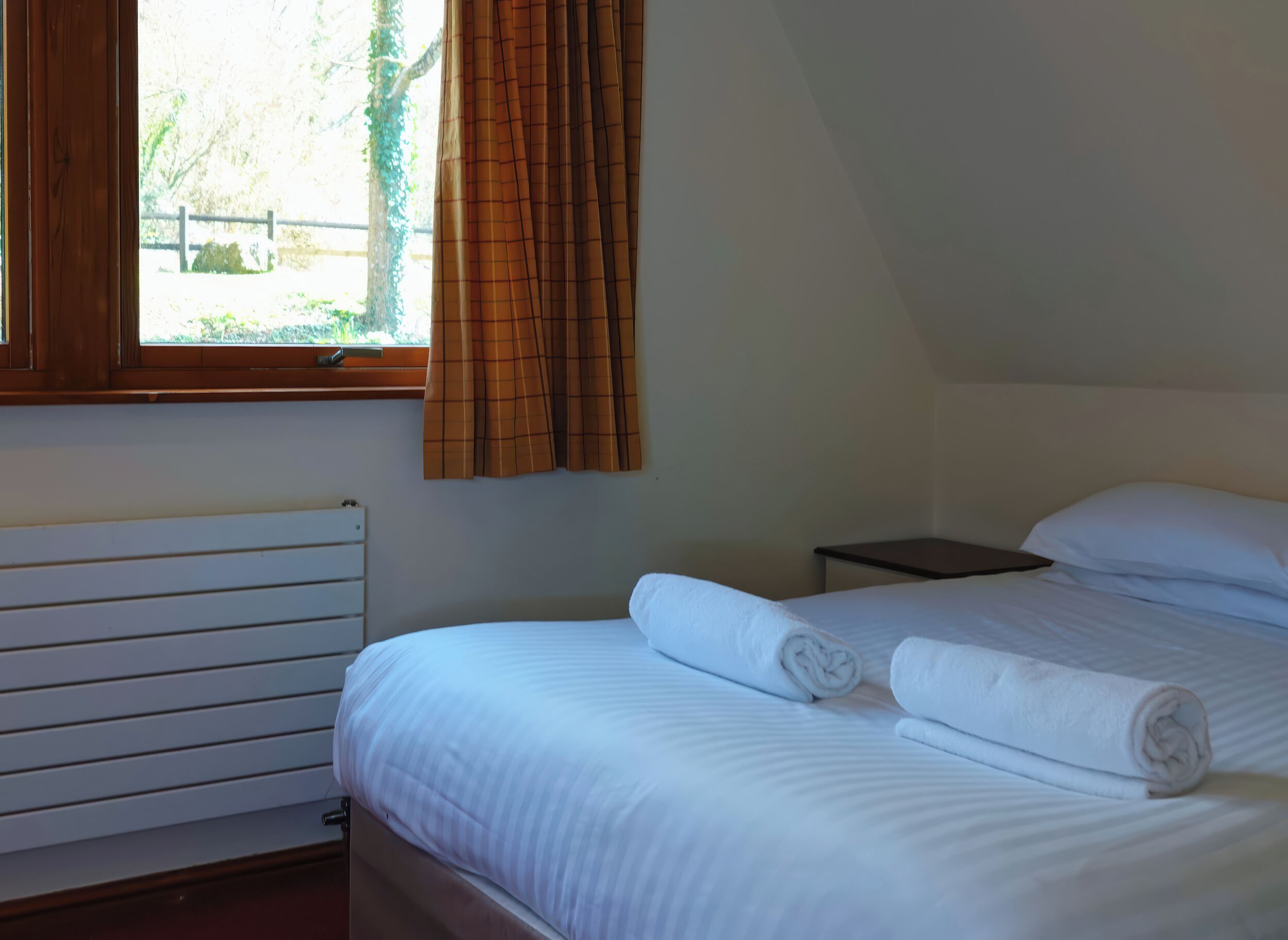 Une chambre à coucher avec un lit, une table de chevet, une fenêtre avec des rideaux et un radiateur.