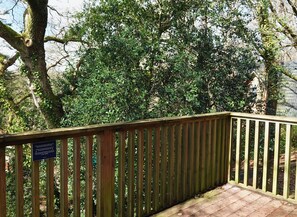 Une terrasse en bois dotée d’une rambarde, entourée d’une végétation luxuriante et d’arbres.