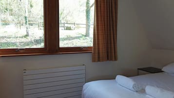 Un dormitorio con cama, mesita de noche, ventana con cortinas y radiador.