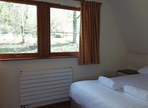 Un dormitorio con cama, mesita de noche, ventana con cortinas y radiador.