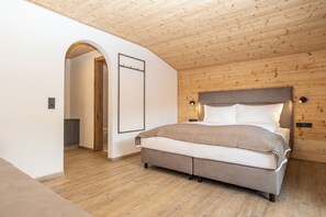 Une chambre avec un plafond en bois, un lit doté d’une tête de lit grise et un mur blanc orné d’un tableau encadré.