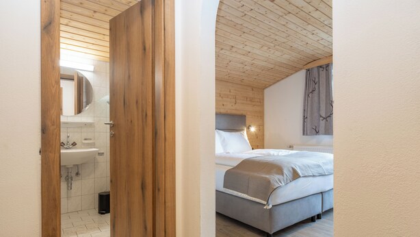 A bedroom with a bed, a nightstand, a mirror, and a window with curtains. - Hofers Herzstück (Hinterglemm)