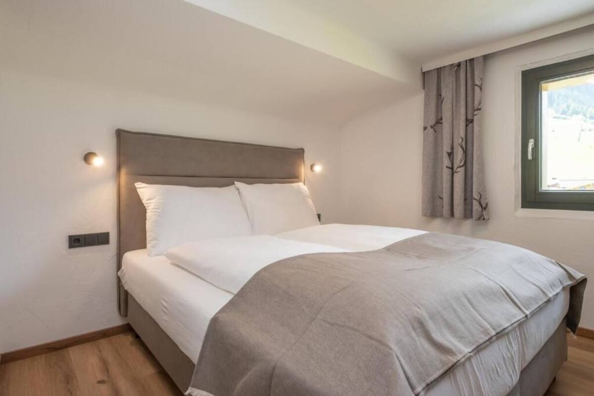 A bedroom with a bed, a headboard, a window with curtains, and a wall-mounted light.