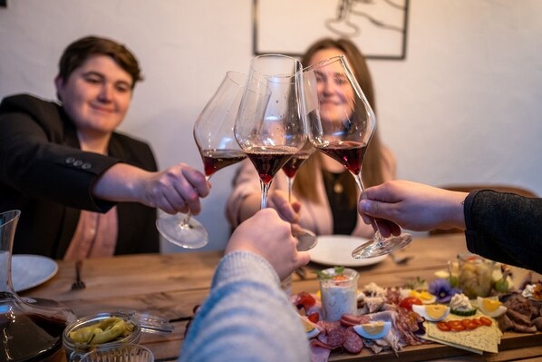 Un groupe de personnes trinquant avec des verres de vin autour d’une table où se trouve une planche de charcuterie.