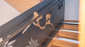 A staircase with a metal railing featuring floral and snowflake designs, leading to a wooden floor. - Hofers Herzstück (Hinterglemm)